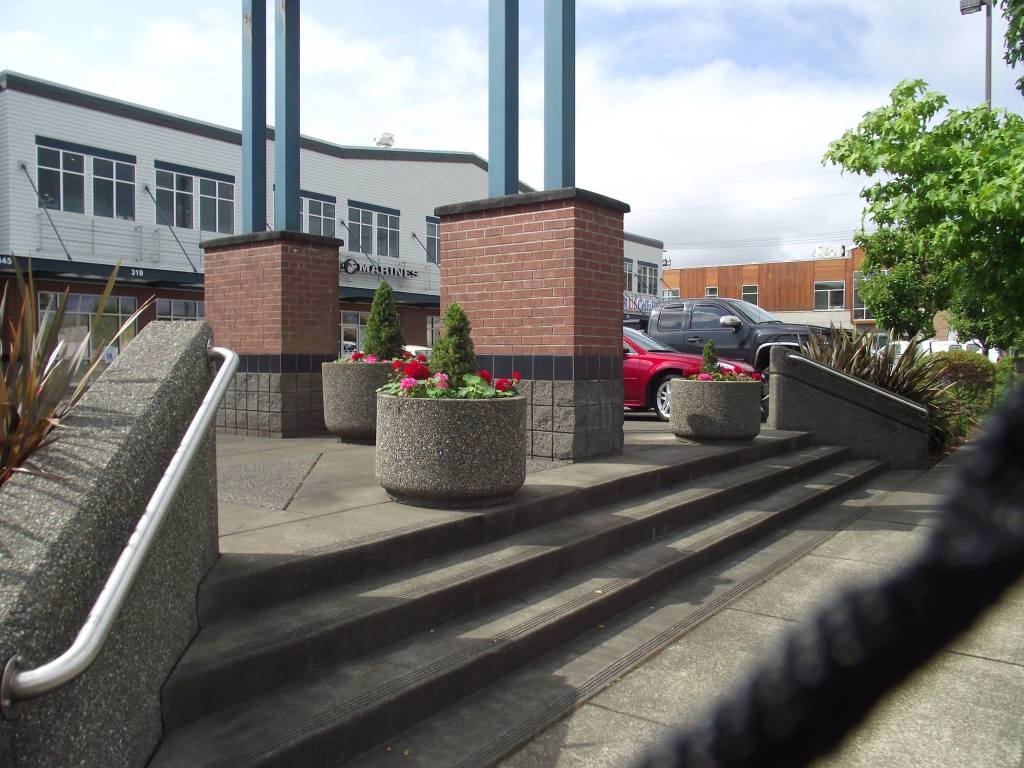 3 Round pots holding pink and red flowers and small bushes near stairs